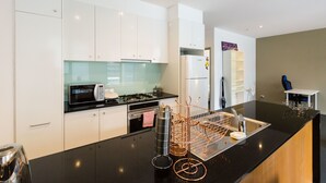 Una cocina moderna con armarios blancos, encimera negra, electrodomésticos de acero inoxidable y salpicadero negro.