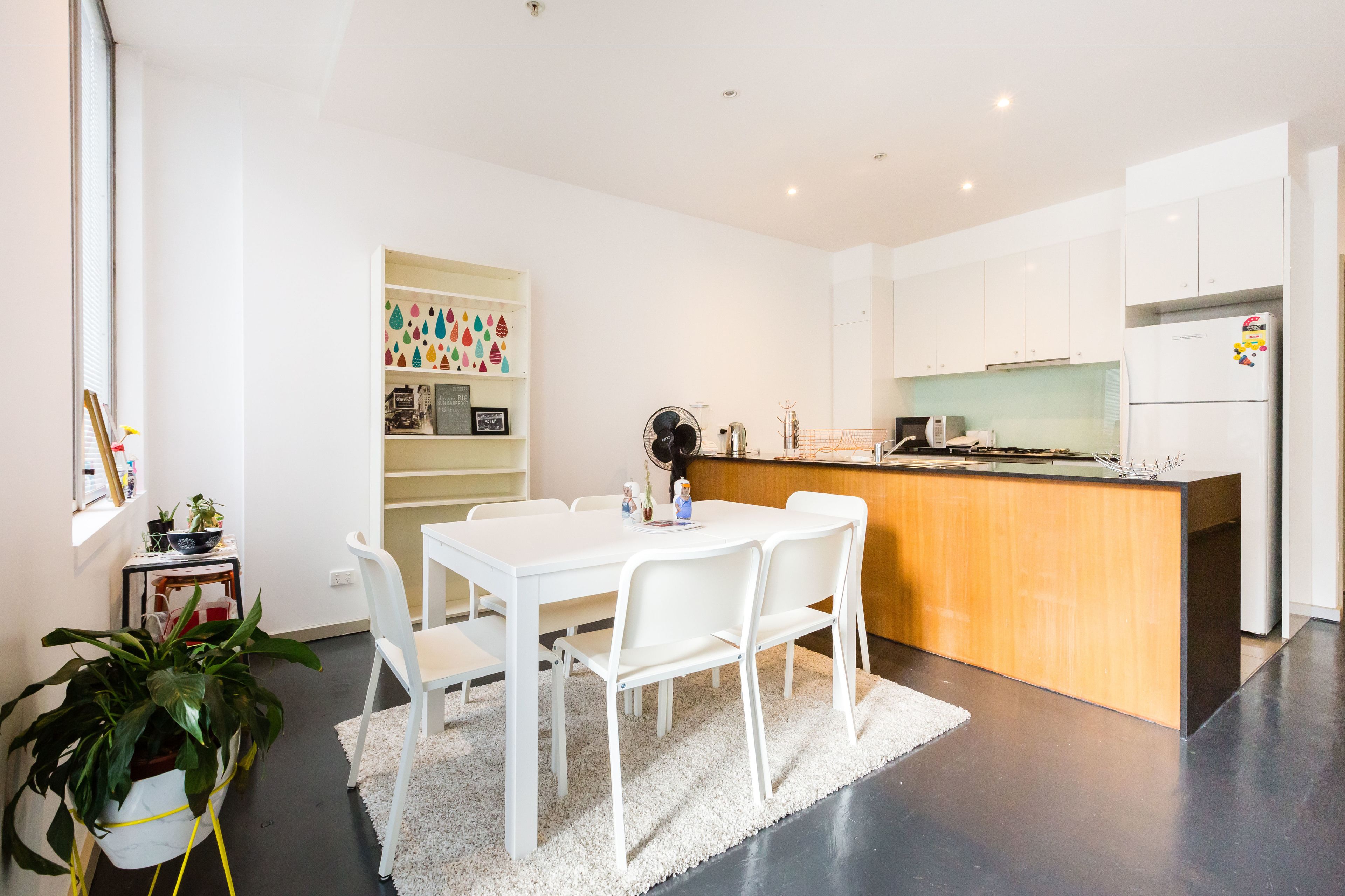 Una cocina moderna con armarios blancos, una isla de madera y un comedor con mesa y sillas blancas.