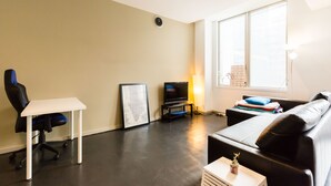 Una sala de estar moderna con un televisor de pantalla plana, una silla gamer, un sofá y una pequeña mesa.
