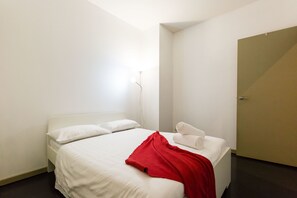 Habitación de hotel minimalista con cama, paredes blancas y una puerta.