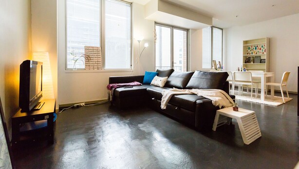 Una sala de estar moderna con un sofá de cuero negro, una mesita blanca y un televisor sobre un mueble.