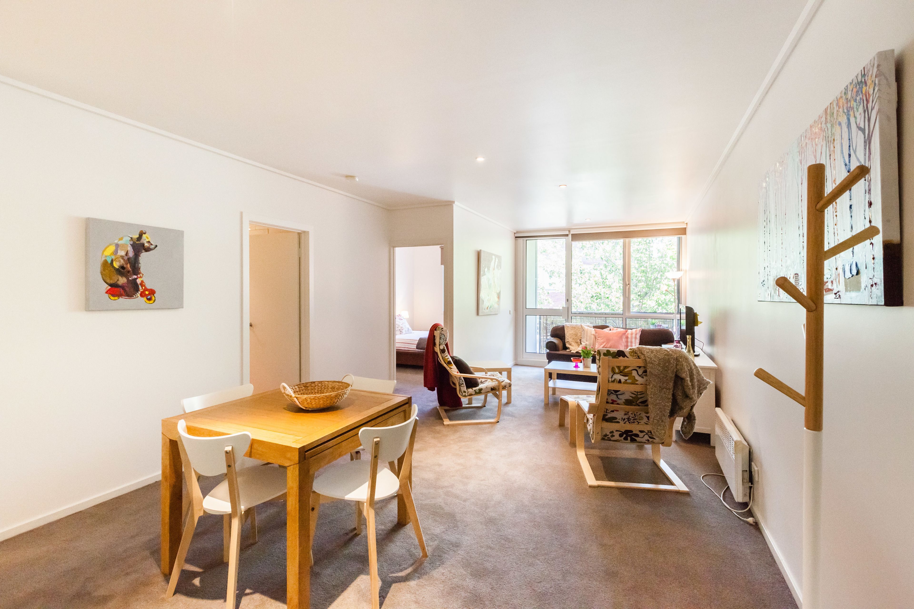 A spacious living area with a dining table, chairs, a sofa, and a large window providing natural light.