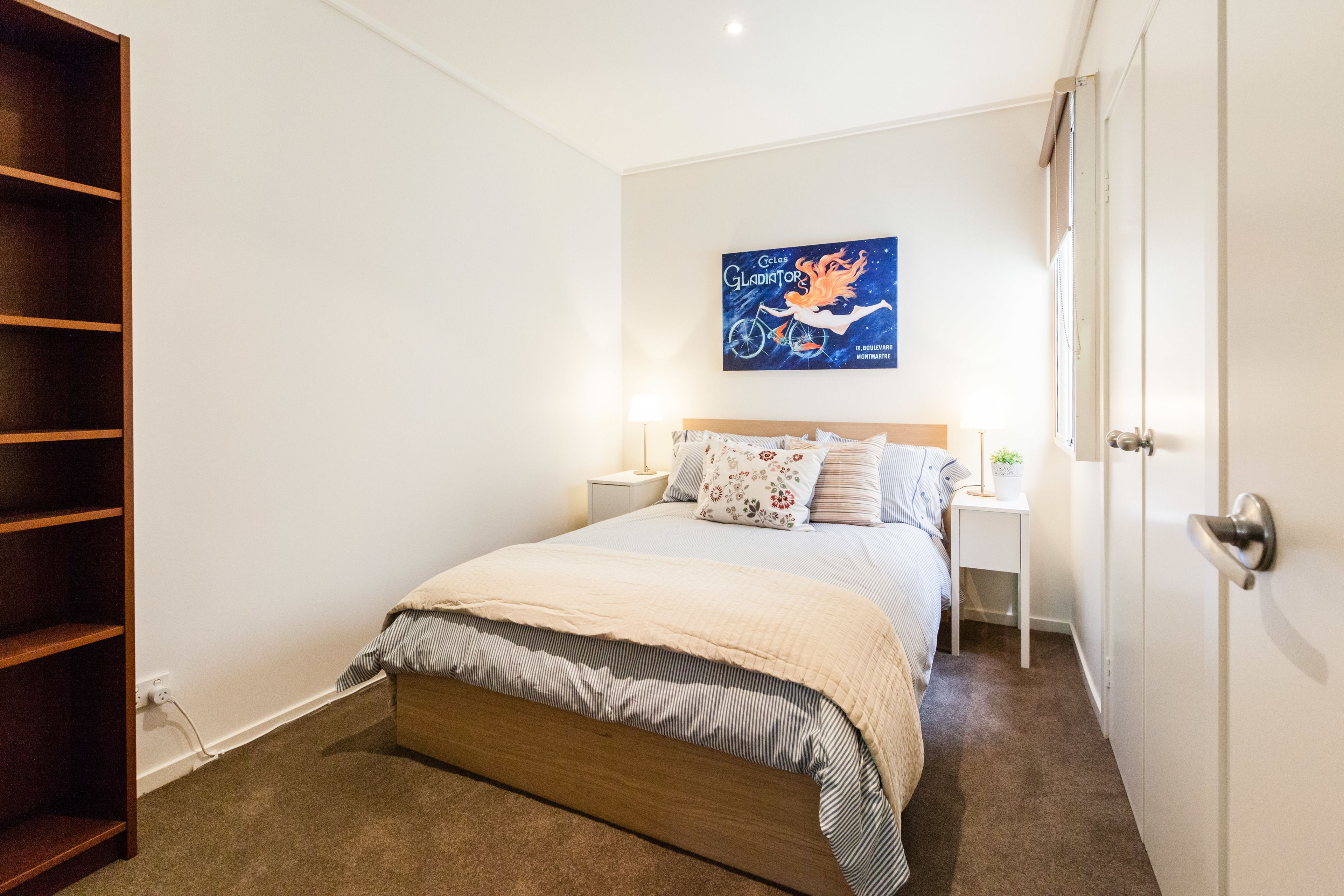 Un dormitorio con cama, mesitas de noche, una obra de arte en la pared y un armario.