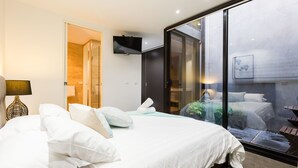 A modern bedroom with a large bed, a flat-screen TV, and a sliding glass door leading to a balcony with a view of the city. - RENEE, 4BDR North Melbourne House (North Melbourne)