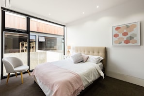 A bedroom with a bed, a chair, a large window, and a wall-mounted artwork. - RENEE, 4BDR North Melbourne House (North Melbourne)
