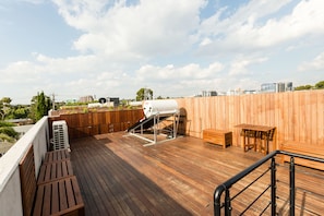 Una terraza en la azotea con una parrilla, mobiliario de madera y vistas al horizonte de la ciudad.
