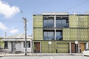 Un edificio moderno con fachada verde, grandes ventanales y una entrada visible con una puerta marcada con el número 32.