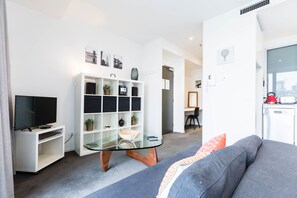 Un salon moderne doté d’un téléviseur à écran plat, d’une table basse en verre, d’un canapé et d’une étagère blanche où sont disposés des objets décoratifs.