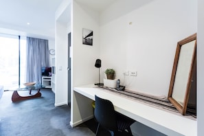 Un espace de vie moderne et compact, comprenant un bureau blanc, un grand miroir et une petite plante en pot.