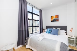 Une chambre d’hôtel moderne avec un grand lit, une table de chevet, une lampe et un tableau au mur.