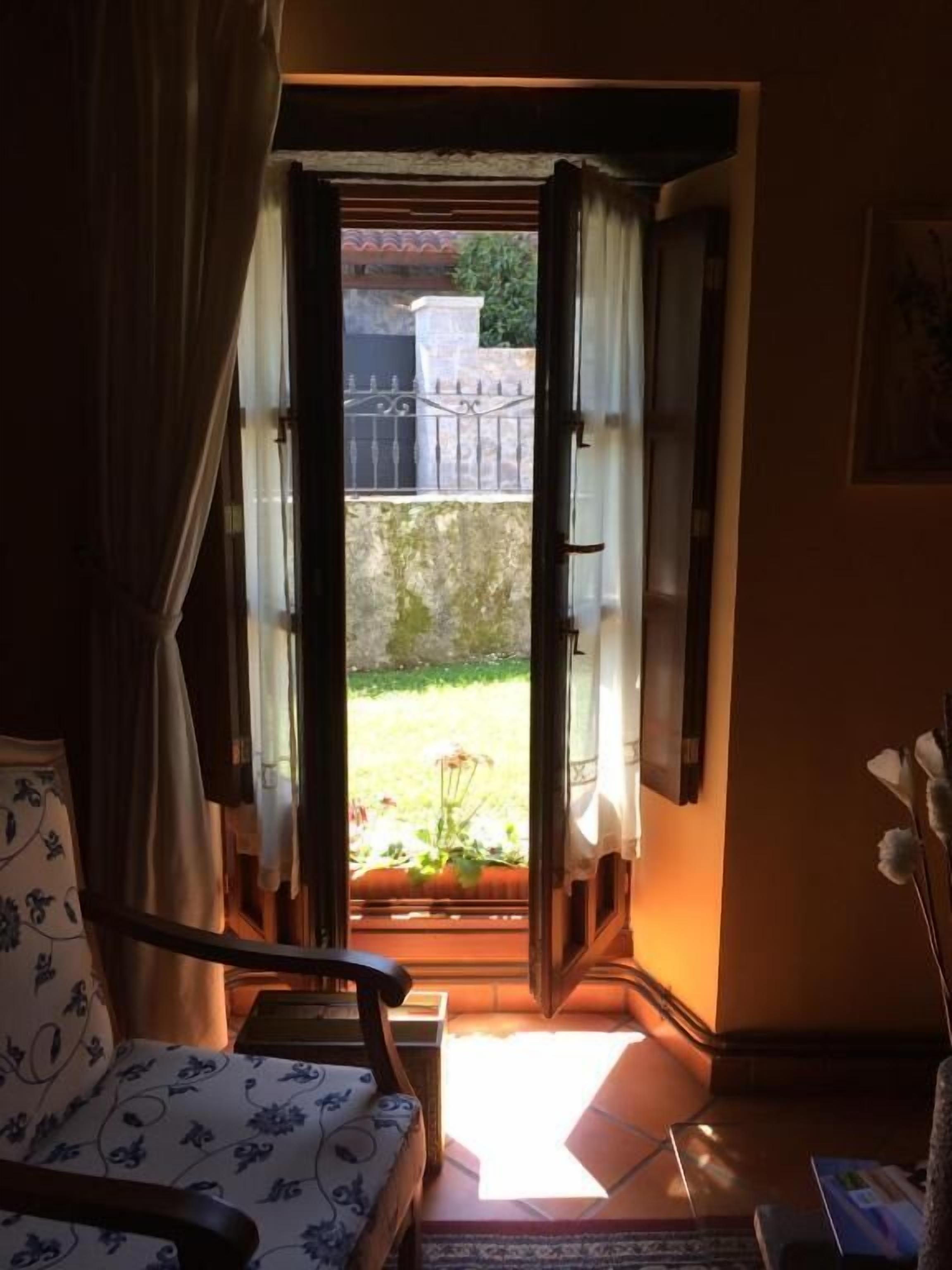 Una habitación con cama, una silla y vistas a un jardín por una puerta abierta.