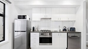 A modern kitchen with white cabinets, a stainless steel refrigerator, a built-in oven, a gas stove, and a dishwasher. - SIENNA, 1BDR South Melbourne Apartment (South Melbourne)