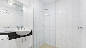 A modern bathroom with a white sink, mirror, and shower. - SIENNA, 1BDR South Melbourne Apartment (South Melbourne)