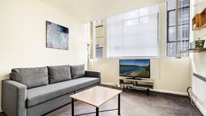 A living room with a grey sofa, a wooden coffee table, a flat-screen TV, and a painting on the wall. - SIENNA, 1BDR South Melbourne Apartment (South Melbourne)