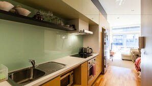 Een moderne keuken met een roestvrijstalen spoelbak, een magnetron en een oven. Er is een houten aanrecht en uitzicht op de woonkamer.