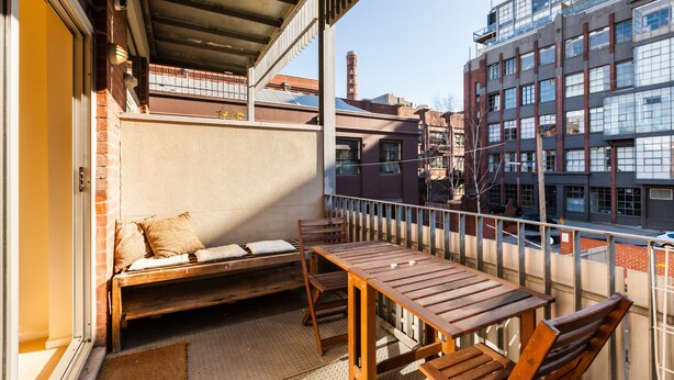 Een balkon met een houten tafel en stoelen, een bank met kussens, en uitzicht op de stadsgezicht.