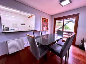 Un comedor con una mesa y sillas de vidrio, una cocina con baldosas blancas y un ventanal con vistas.