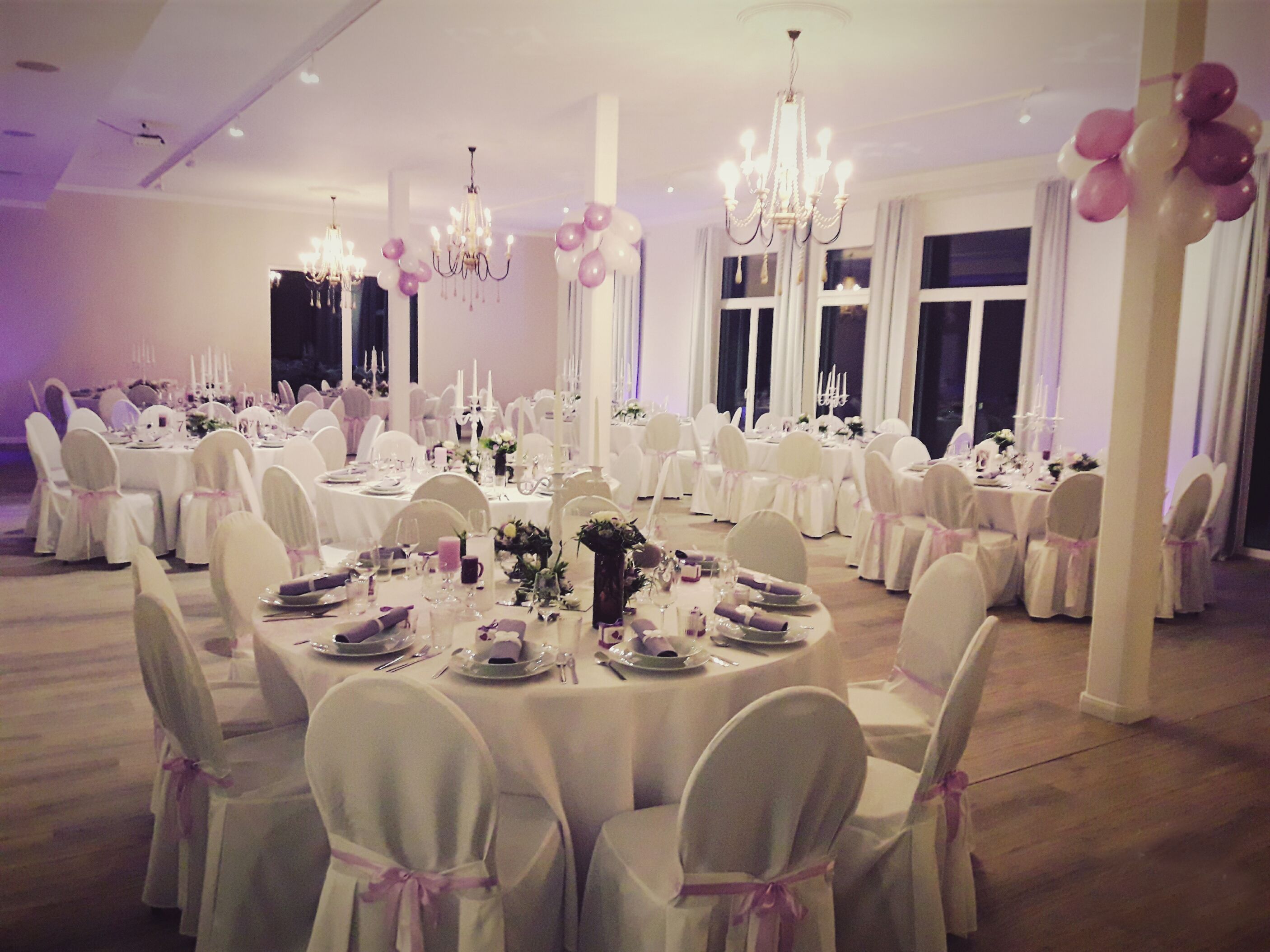 A banquet hall with round tables, white tablecloths, and chairs with pink sashes.