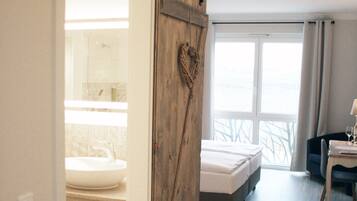 Quarto de hotel com porta de madeira deslizante, cama, escrivaninha com cadeira e vista para o exterior.