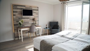 A modern hotel room with a large bed, a desk with a chair, a small table with a bottle and glasses, and a view of the outdoors. - Trautwein - Das Winzerhotel am La Roche (Flonheim)