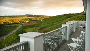 A balcony with white chairs, a view of a vineyard, and a road in the distance. - Trautwein - Das Winzerhotel am La Roche (Flonheim)