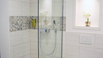 Un baño moderno con ducha de vidrio, inodoro y un pequeño ventanal con una flor.