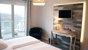 A hotel room with a bed, a desk with a chair, a TV mounted on a wood-patterned wall, and a balcony with a view.