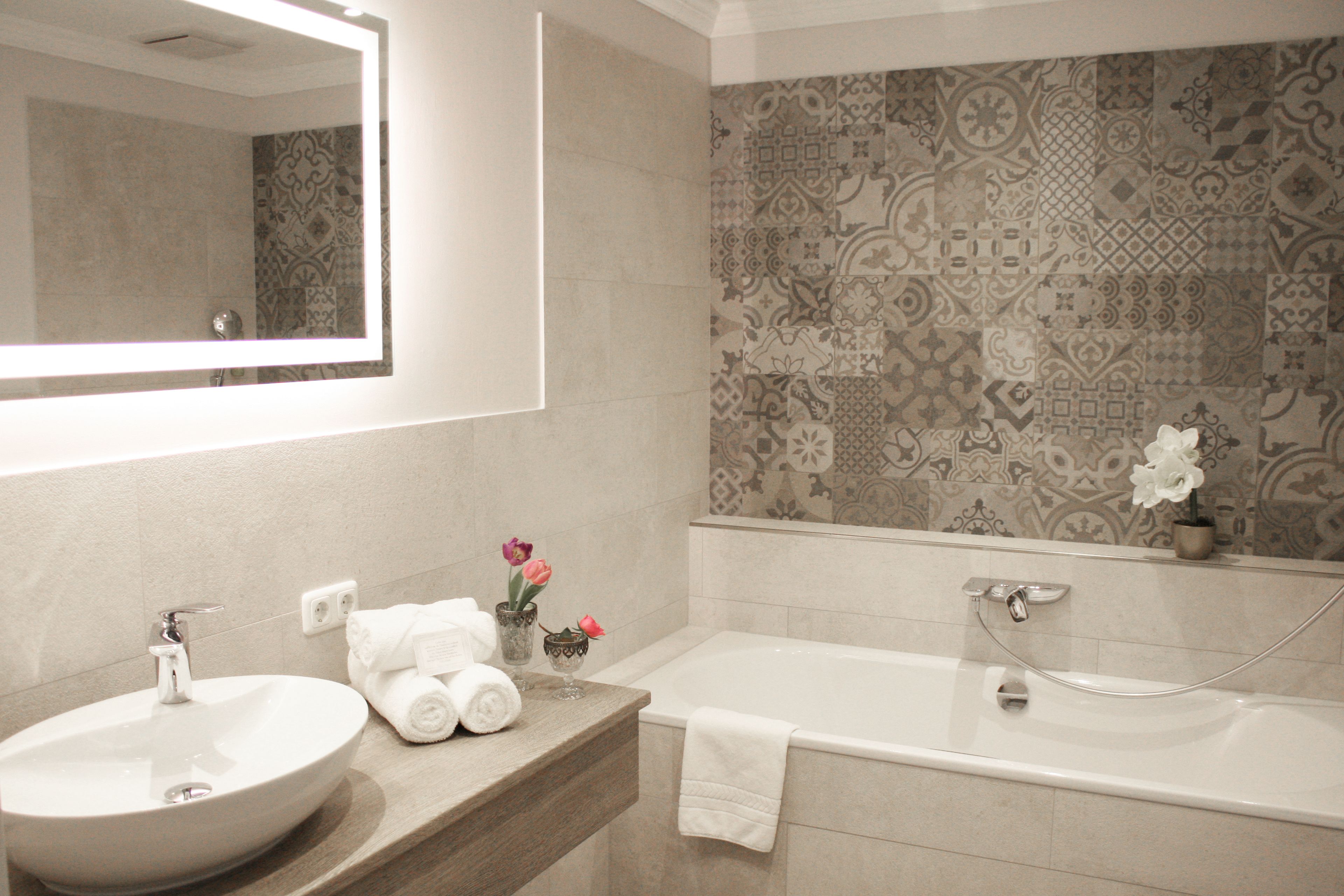Une salle de bain avec un grand miroir, un lavabo, une baignoire et des carreaux décorés.