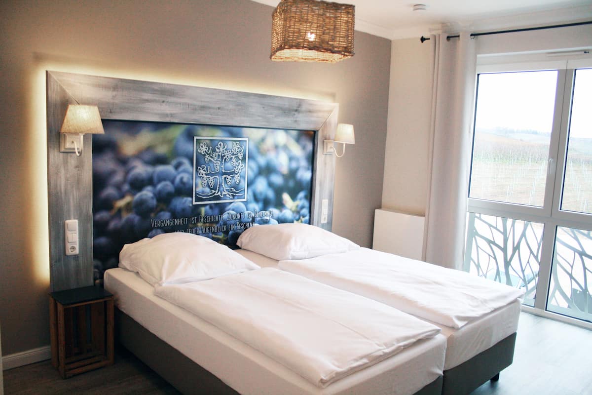 Un dormitorio con una cama grande, un cabecero con una obra de arte con motivos de frutas, dos lámparas de noche y vistas al exterior a través de un ventanal amplio.