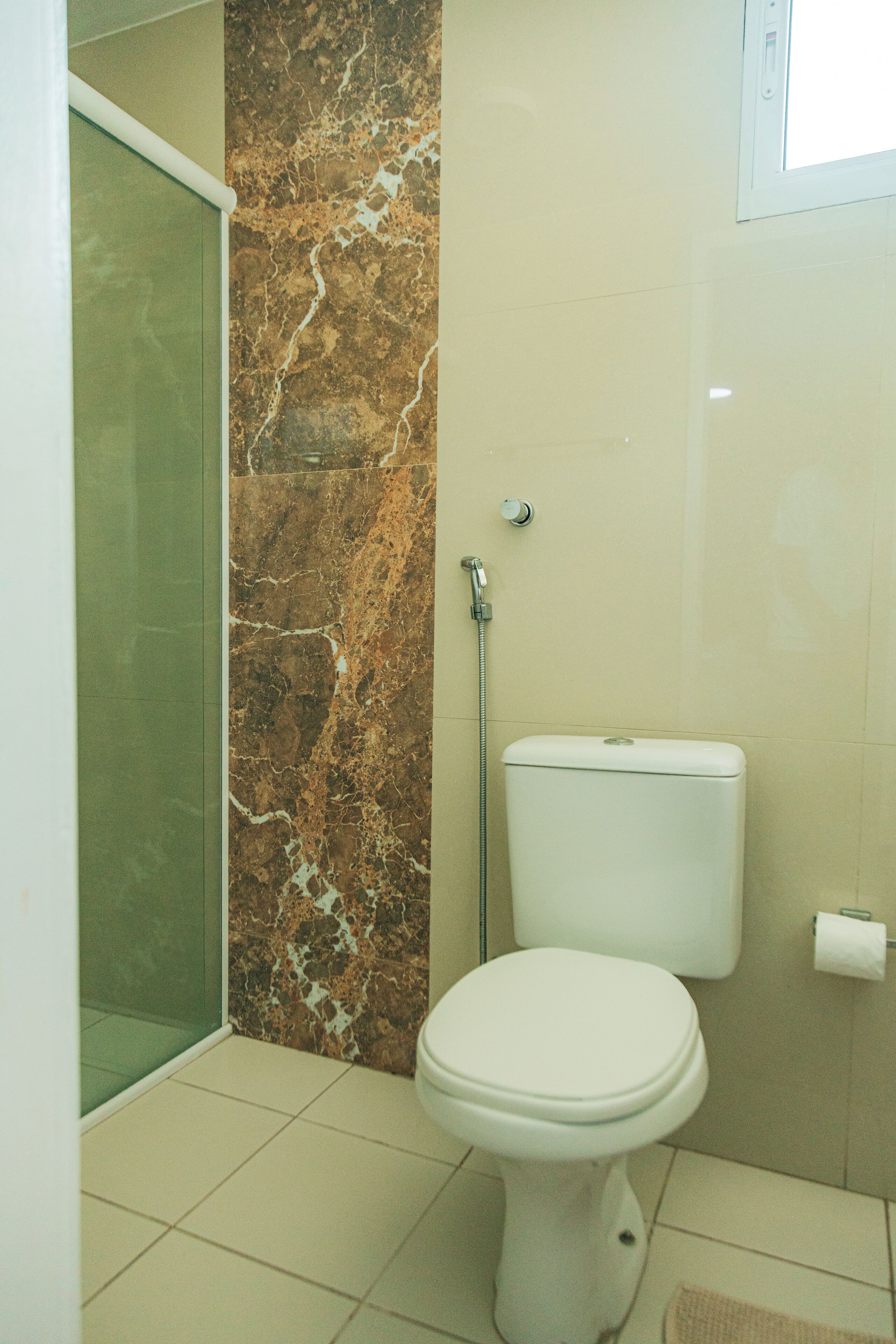 Un baño con inodoro, ducha y pared de mármol.