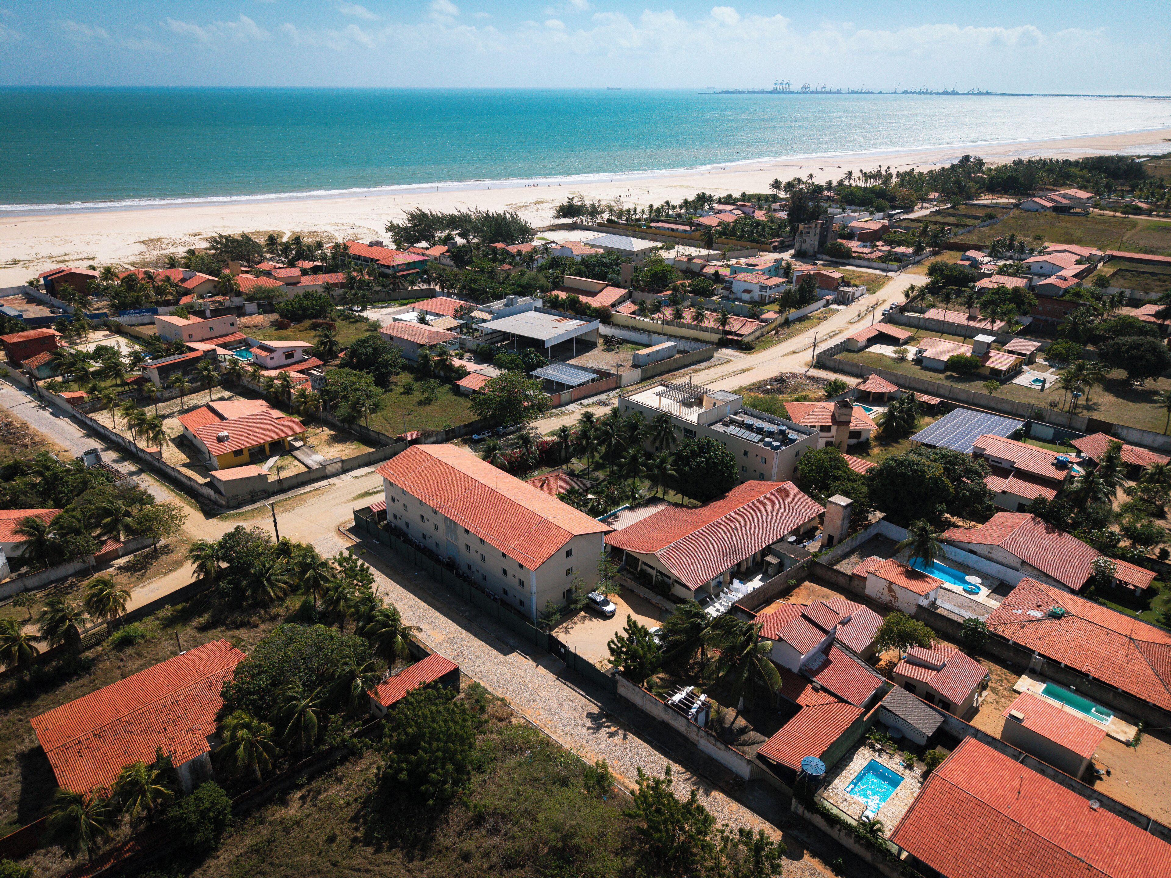 Vue aérienne d’une zone résidentielle côtière, avec des maisons, une plage et un ciel dégagé.