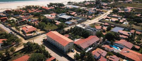 Vue aérienne d’une zone résidentielle côtière, avec des maisons, une plage et un ciel dégagé.