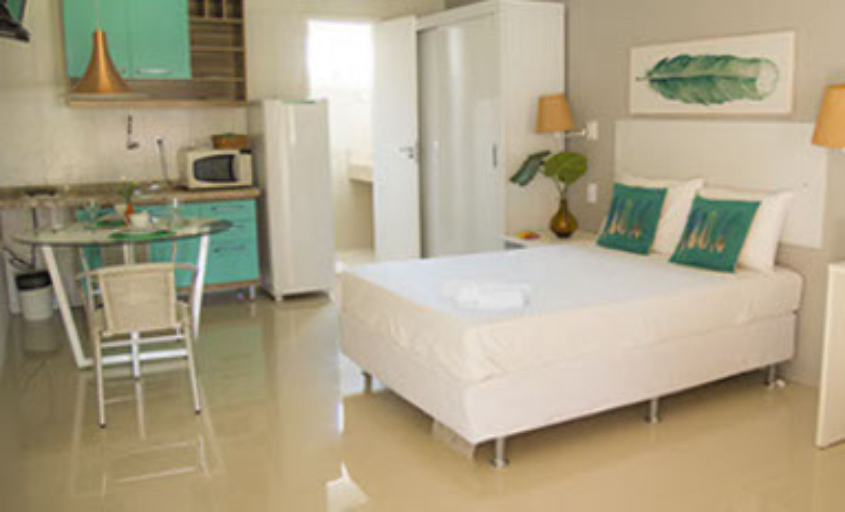 A compact hotel room with a bed, a small kitchenette, a dining table, and a chair.