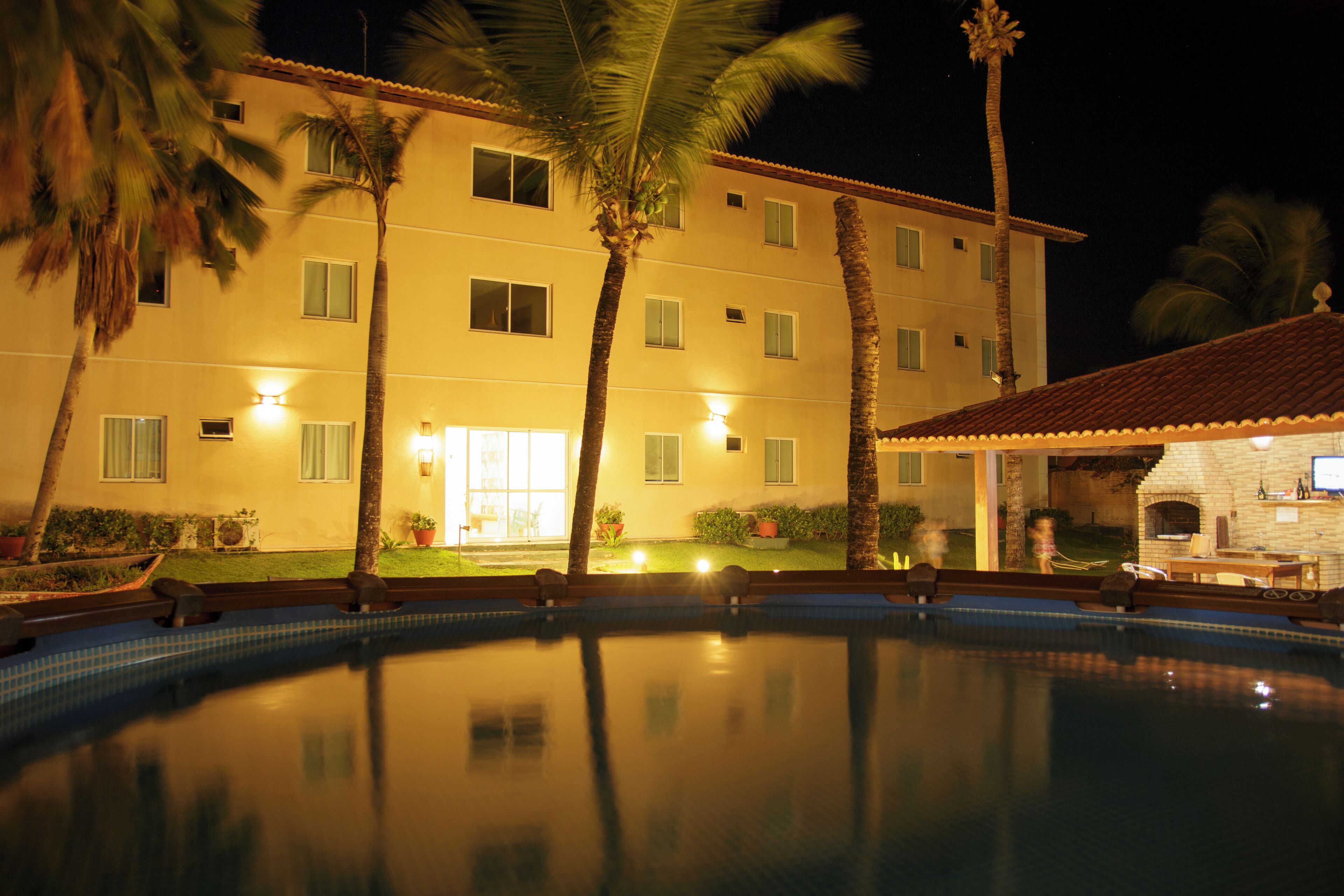 A hotel with a swimming pool, palm trees, and a well-lit exterior.