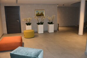 A lobby with a dark door, three white planters with white flowers, a yellow ottoman, and two cushioned seating areas. - Monteverde Hotel (Beit Mery)