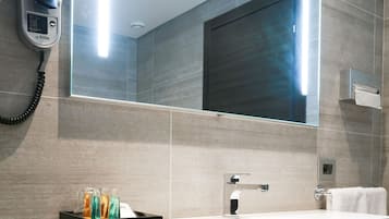 Un baño moderno con un espejo grande, un lavabo blanco, un secador de pelo y un perchero para toallas.