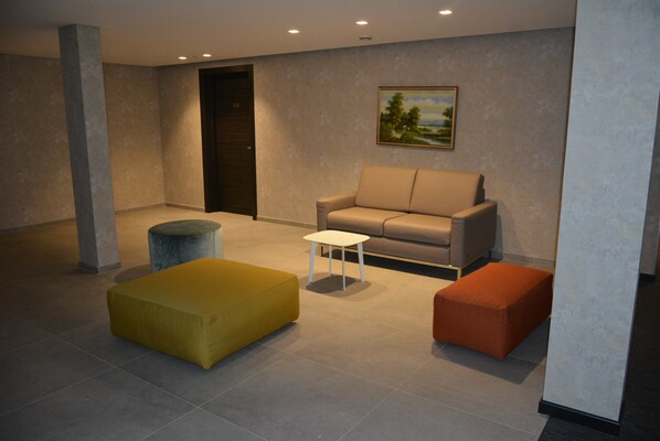 Um lobby moderno com um sofá, um banquinho e uma pequena mesa.