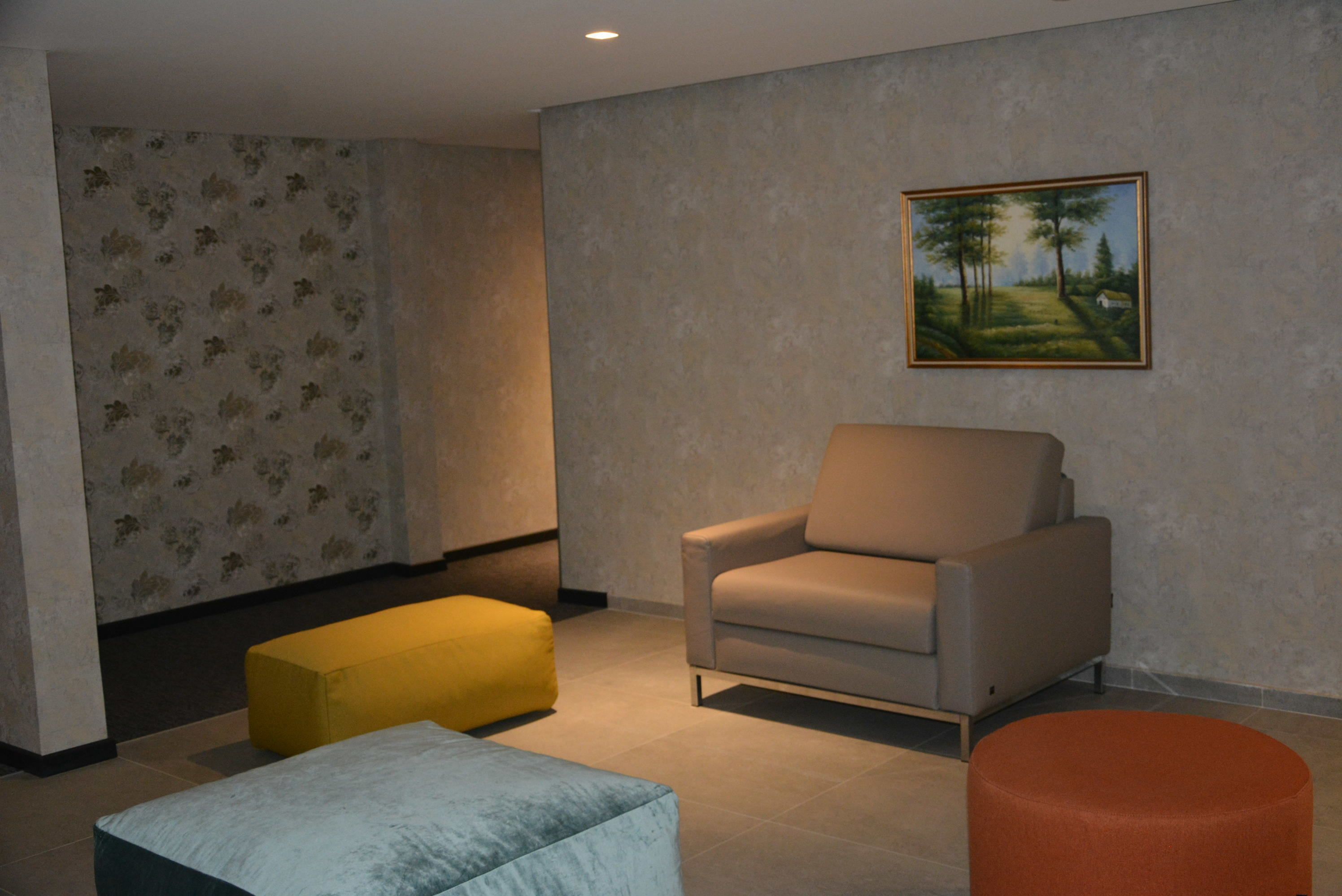 A living room with a beige armchair, a yellow ottoman, and an orange ottoman.