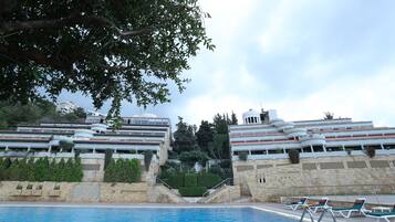 Una piscina con sillones reclinables, una escalera de piedra y edificios modernos al fondo.