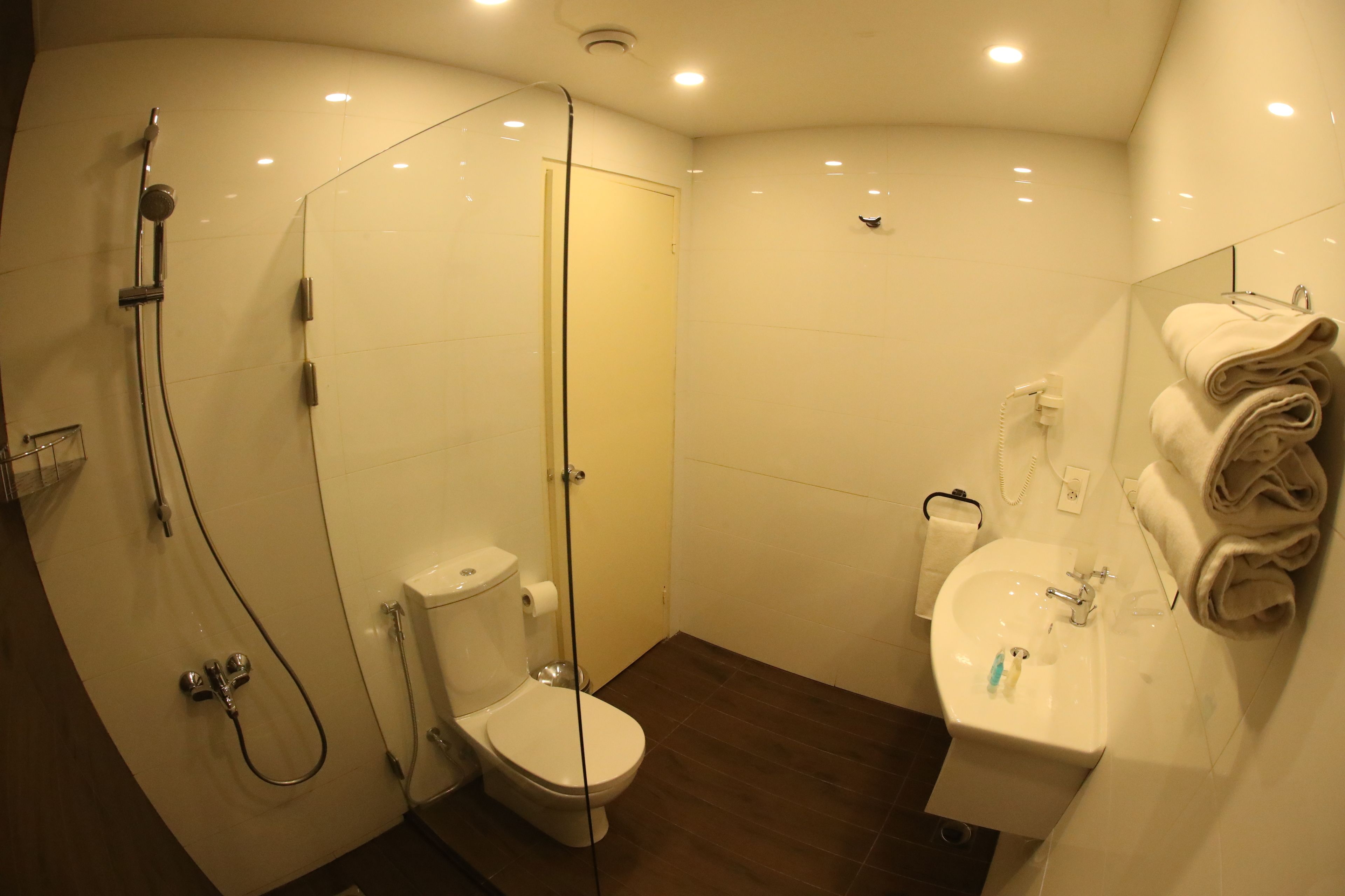 Un bagno con doccia vetro, WC, lavandino e porta asciugamani.
