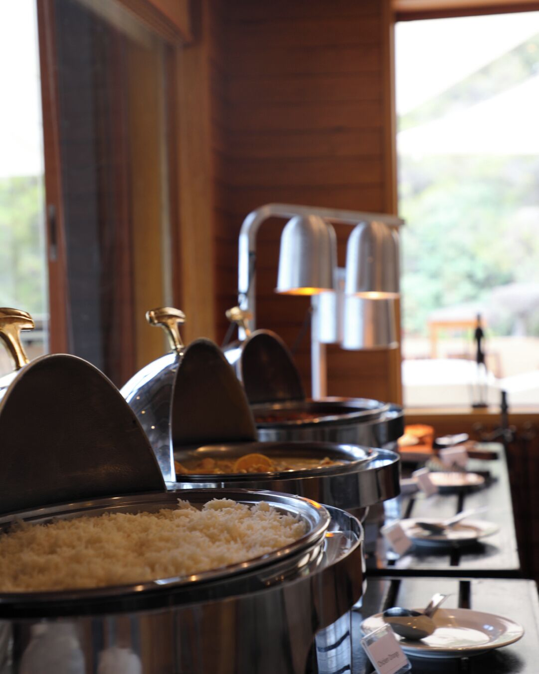 Buffet-style food service with multiple serving stations, each with a metal lid and a spoon.