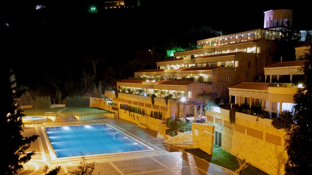 A multi-story hotel with a swimming pool, outdoor seating, and a well-lit facade. - Monteverde Hotel (Beit Mery)