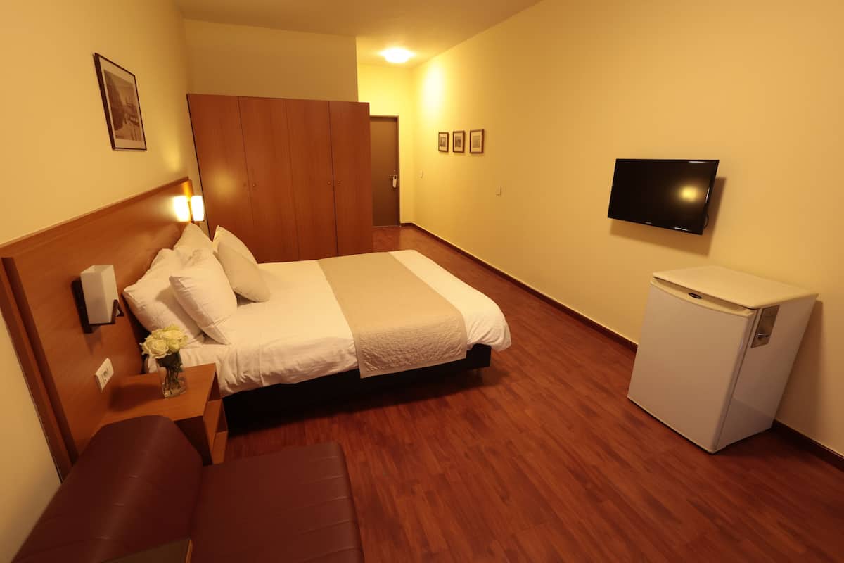 Habitación de hotel con cama, una mesita con un florero, un banco, un armario, televisor y refrigerador.