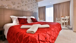 A hotel room with a large bed, a small table with chairs, and a view of the city through the window. - Monteverde Hotel (Beit Mery)