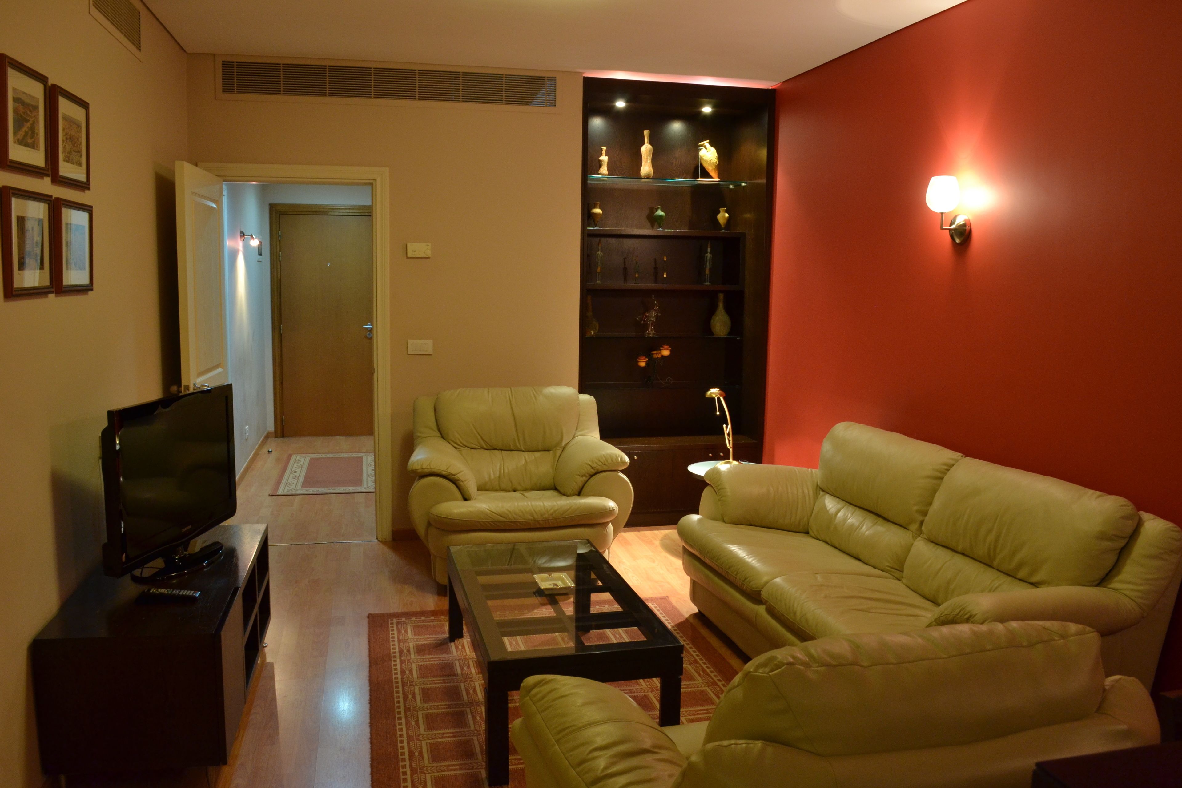 A living room with a television, two leather sofas, a coffee table, and a bookshelf with decorative items.