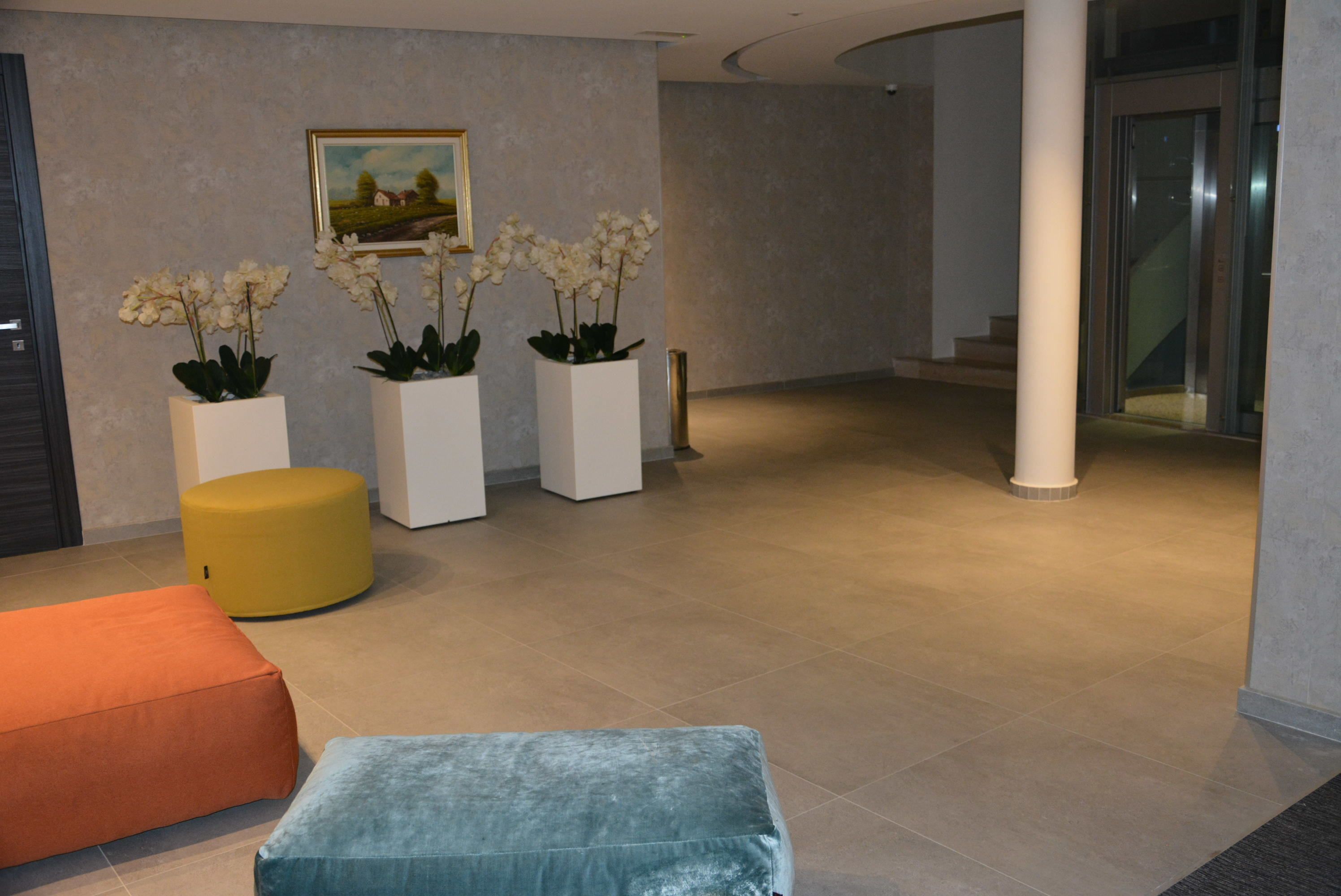 A lobby with a reception desk, three white planters with white flowers, a yellow ottoman, and a blue cushioned bench.