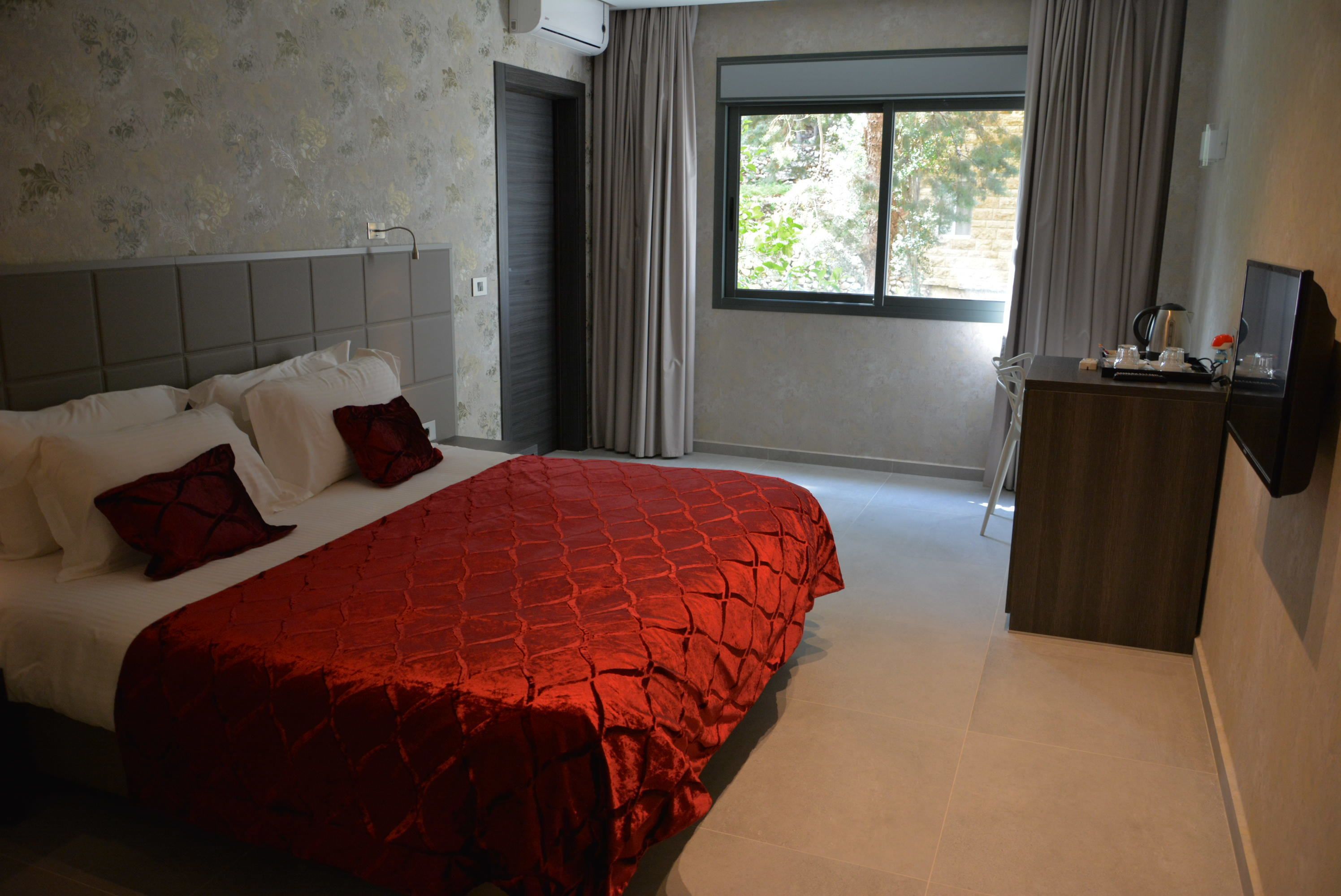 A bedroom with a large bed, a desk, and a window with curtains.