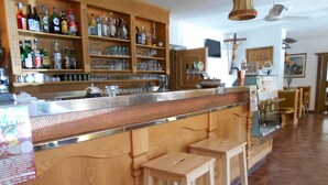 Un espace bar avec des étagères en bois remplies de bouteilles et de verres, un comptoir et des tabourets.