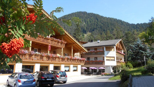 Un bâtiment traditionnel en bois, doté de balcons, d’un espace de stationnement et surplombant un paysage montagneux.