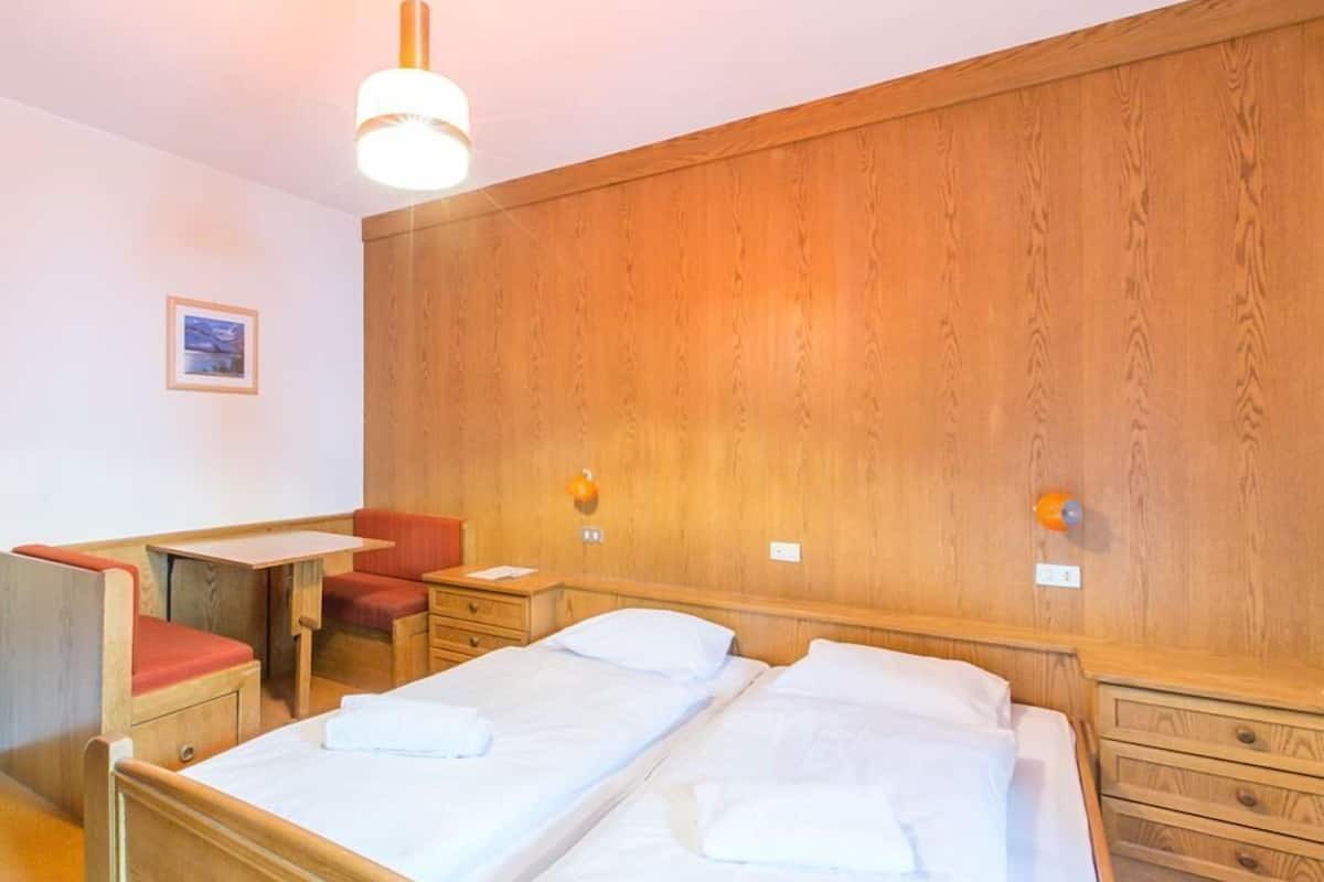Une chambre d’hôtel avec deux lits, un bureau, une chaise et des lambris en bois sur les murs.